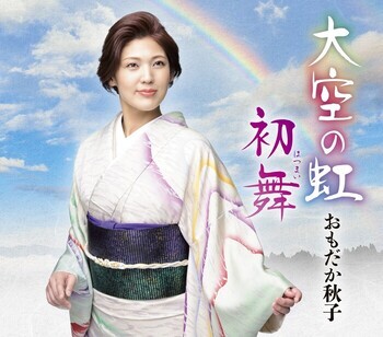 おもだか秋子さんが虹がかかる青空の背景のもと、微笑んでいるアーティスト写真です。また、生ライブで披露される大空の虹・初舞の記載があります。