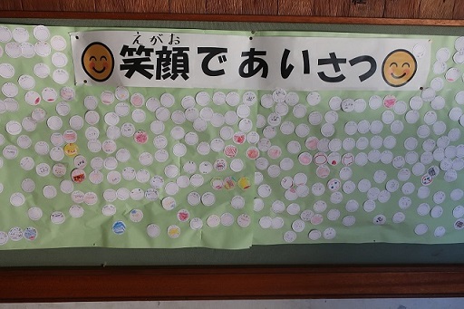「笑顔であいさつ」と記載され、児童がたくさんのシールを貼っている掲示ボードの写真