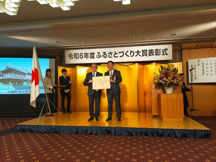 写真：賞状を持ち、写真撮影に応じる川越町並み委員会　原委員長
